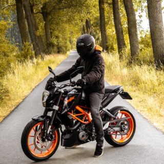 man riding black and orange motorcycle beside trees