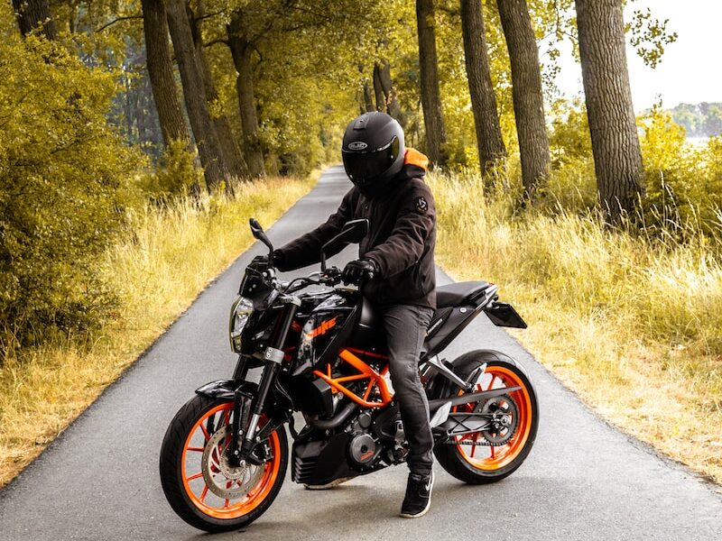 man riding black and orange motorcycle beside trees