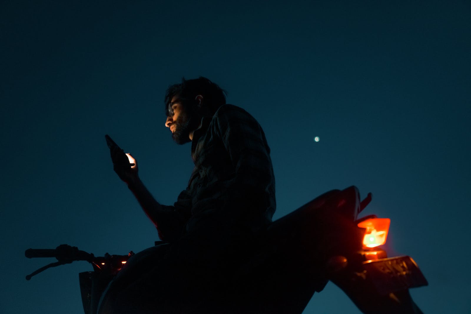 Man Sitting with Cellphone on Motorbike at Night