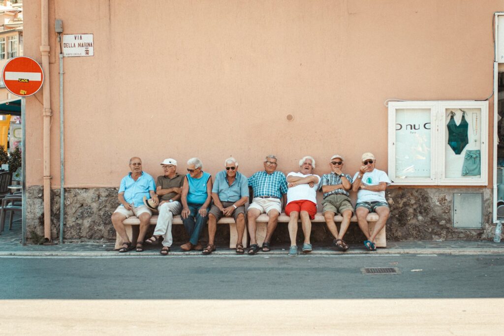 eight men sitting on bench near orange wall during daytime