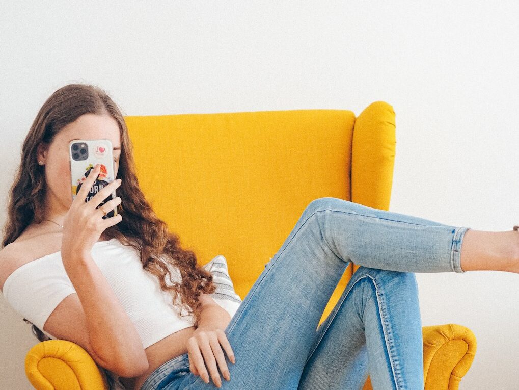 woman in white tank top and blue denim jeans sitting on yellow sofa
